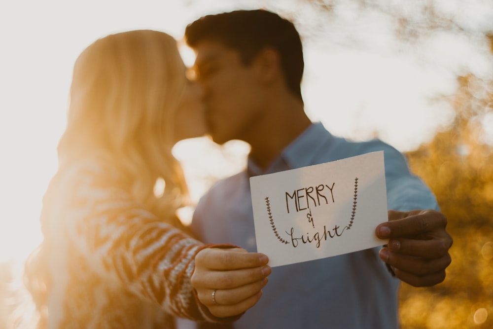 couple kissing while holding merry and bright signage