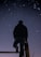 A person stands on a raised platform, gazing at a clear night sky filled with stars. The silhouette of the individual creates a striking contrast against the backdrop of the twinkling celestial bodies.