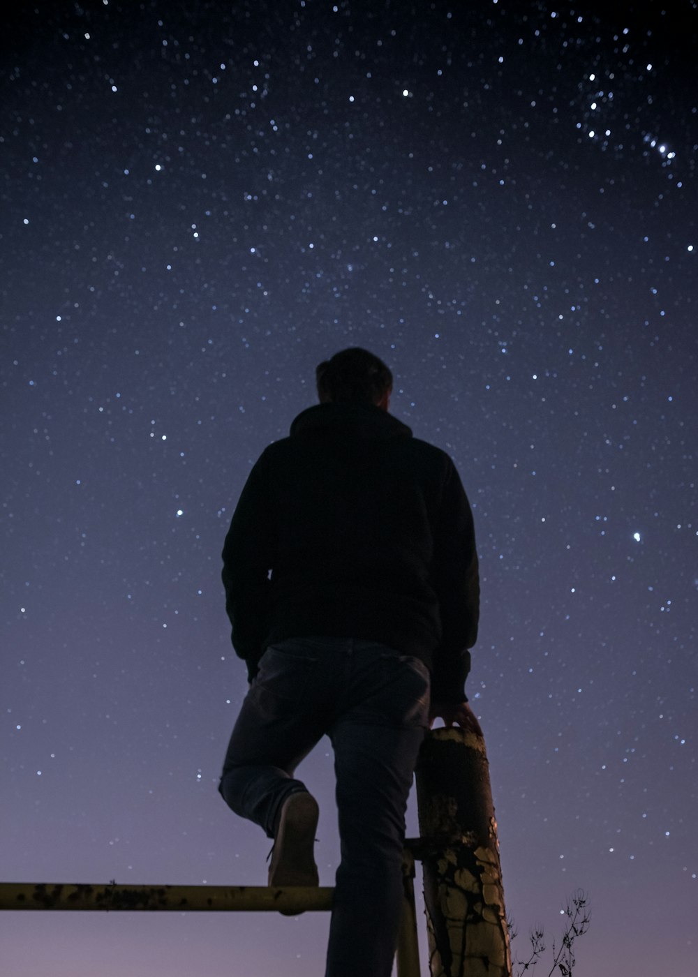 man wearing black hoodie standing near wooden post