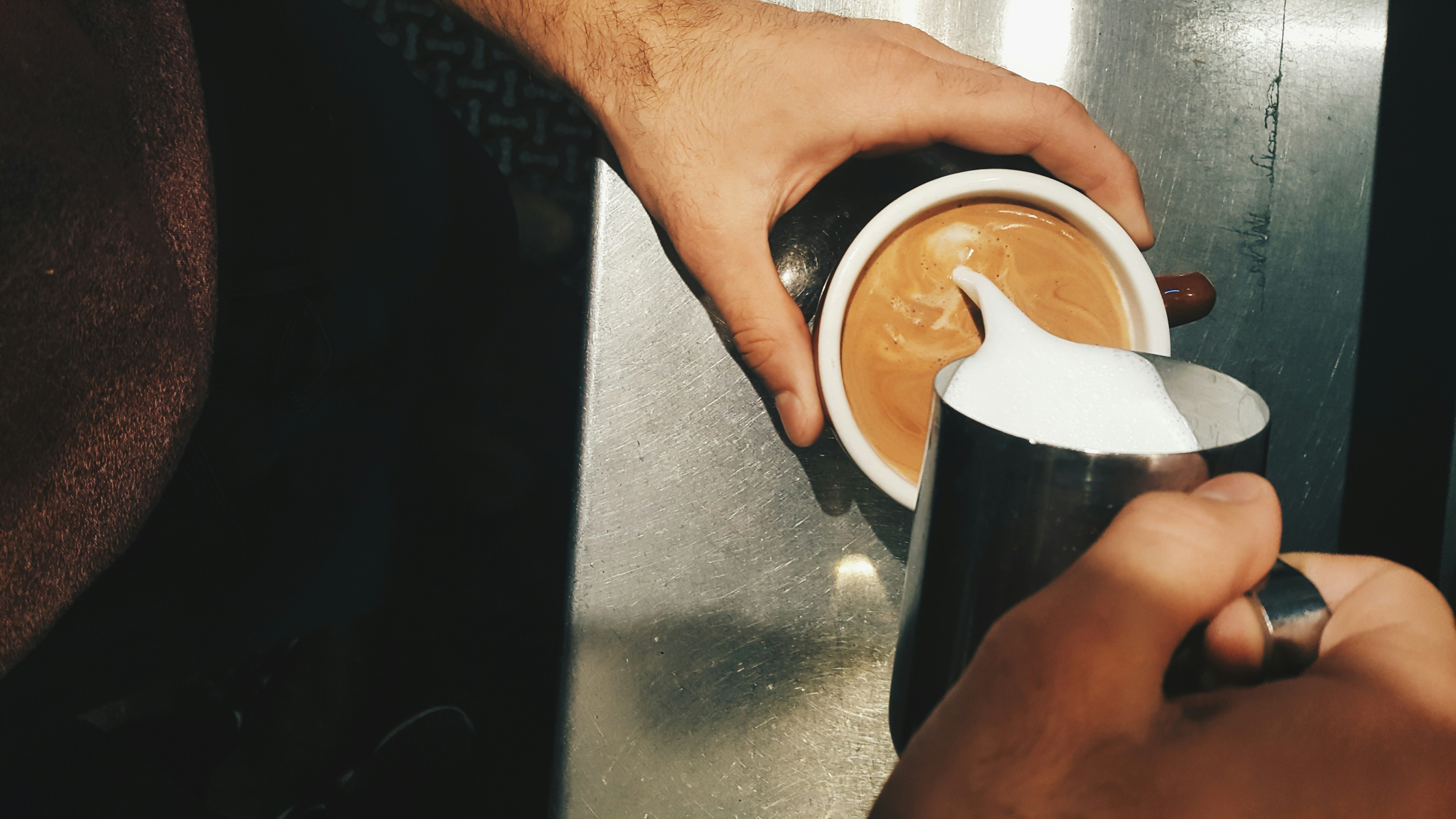 Barista pouring steamed milk into espresso creating beautiful latte art in warm golden light
