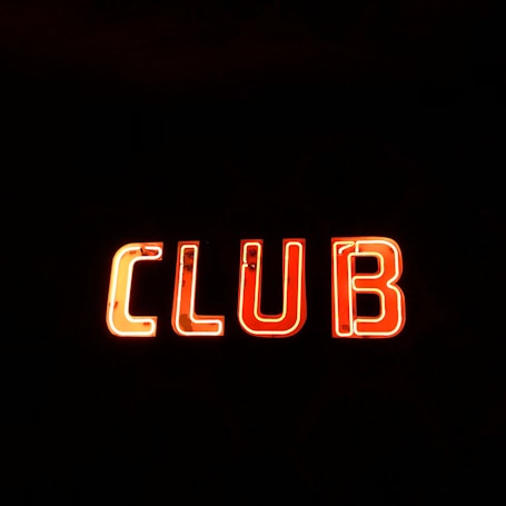 Neon sign displaying the word 'CLUB' in bright, glowing red-orange letters against a stark black background.