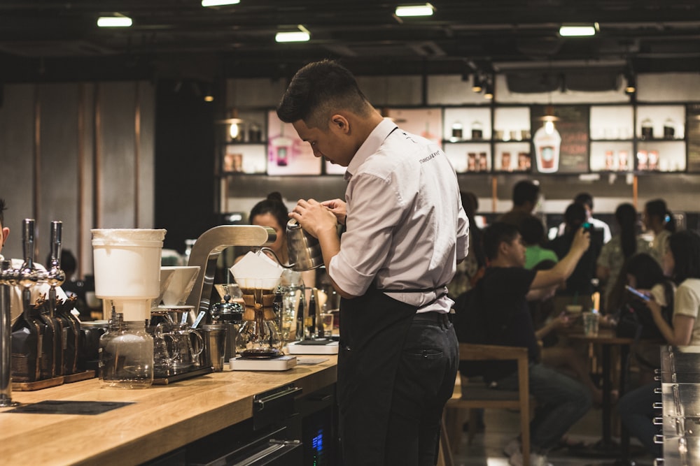 men's brown dress shirt and black pants making drinks inside a bar