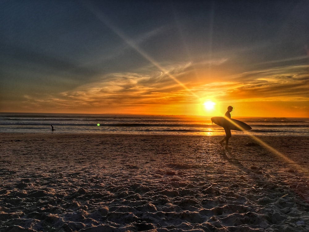 silhouette of person walking on shore during golden hour