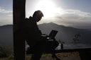 Federico Botero sitting on a rustic wooden bench, notebook in hand, with a sunset over Andean mountains behind him.