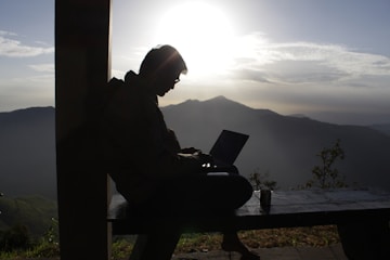 Federico Botero sitting on a rustic wooden bench, notebook in hand, with a sunset over Andean mountains behind him.