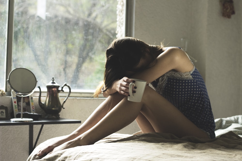 woman sitting on bed while holding mug