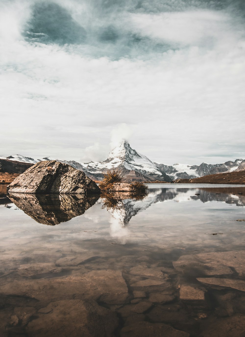 body of water near mountain under white sky