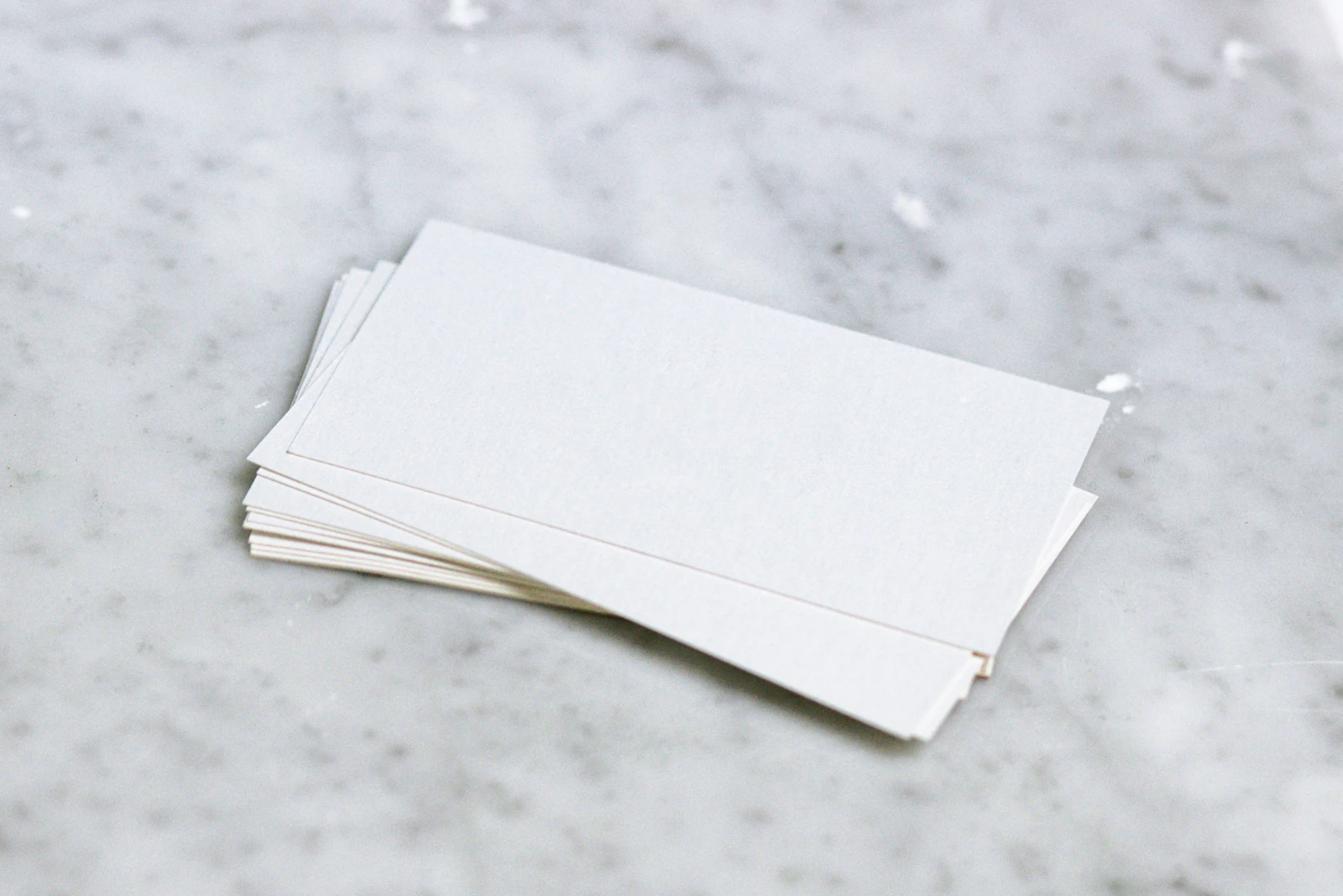 A small stack of white blotter cards on grey marble