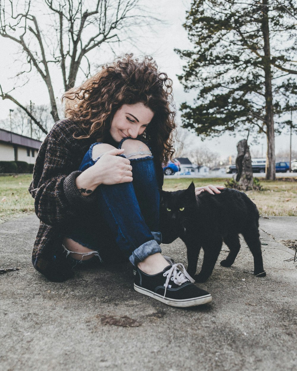 woman sitting on ground while petting cat during daytime