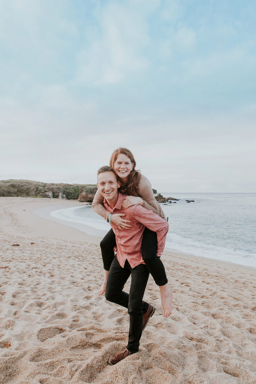 Man carrying a laughing woman on his back by the shore