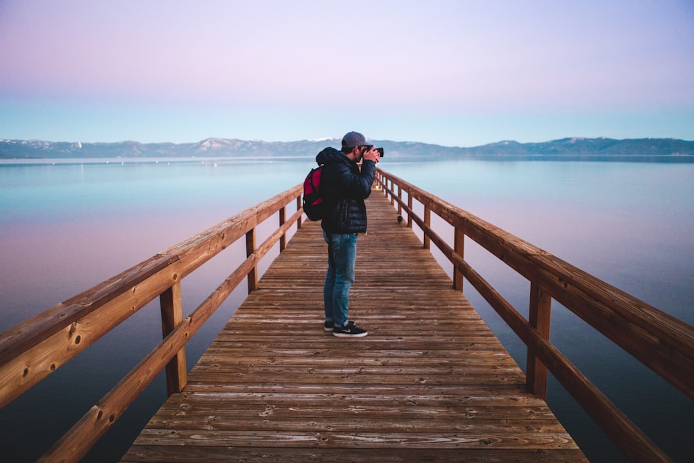 man standing on wood dock taking photo