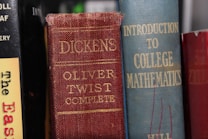 Several books are aligned vertically on a shelf. The visible titles include 'Oliver Twist Complete' by Dickens with a red and worn cover, alongside 'Introduction to College Mathematics' which has a blue cover. Another book with a partially visible title, 'The Eas...', has a yellow and black cover.