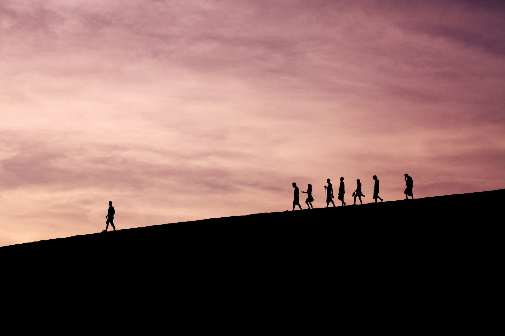 Silhouettes of people walking on a hill. One person is further ahead, leading.