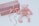 A soft, plush pink teddy bear is placed next to a rectangular, pink glittery gift box wrapped with a pink ribbon and bow. The items are set against a light, neutral background, creating a gentle and serene atmosphere.