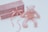 A soft, plush pink teddy bear is placed next to a rectangular, pink glittery gift box wrapped with a pink ribbon and bow. The items are set against a light, neutral background, creating a gentle and serene atmosphere.