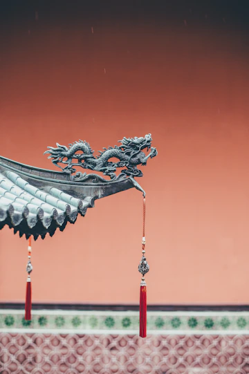 A bronze dragon sculpture on a tiled roof corner with red tassels