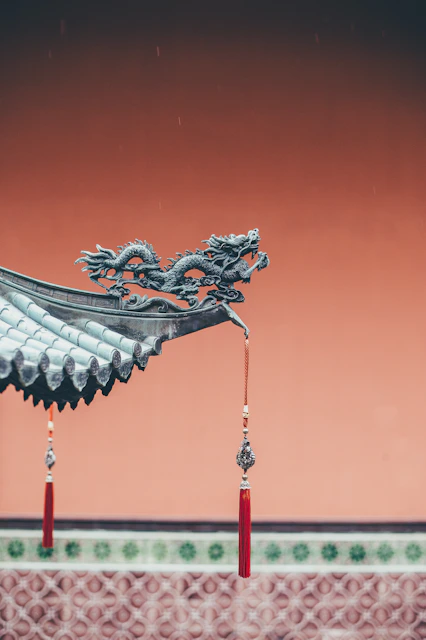 A bronze dragon sculpture on a tiled roof corner with red tassels