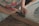 A person is using a tool with a red handle, possibly a staple remover or similar tool, to work on a wooden frame. The person is wearing a shirt with a colorful floral pattern, and their focus appears to be on the task at hand. The setting suggests a crafts or DIY environment.