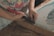 A person is using a tool with a red handle, possibly a staple remover or similar tool, to work on a wooden frame. The person is wearing a shirt with a colorful floral pattern, and their focus appears to be on the task at hand. The setting suggests a crafts or DIY environment.