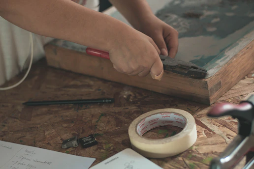 Hand applying fast-drying adhesive on a wooden surface with tools nearby