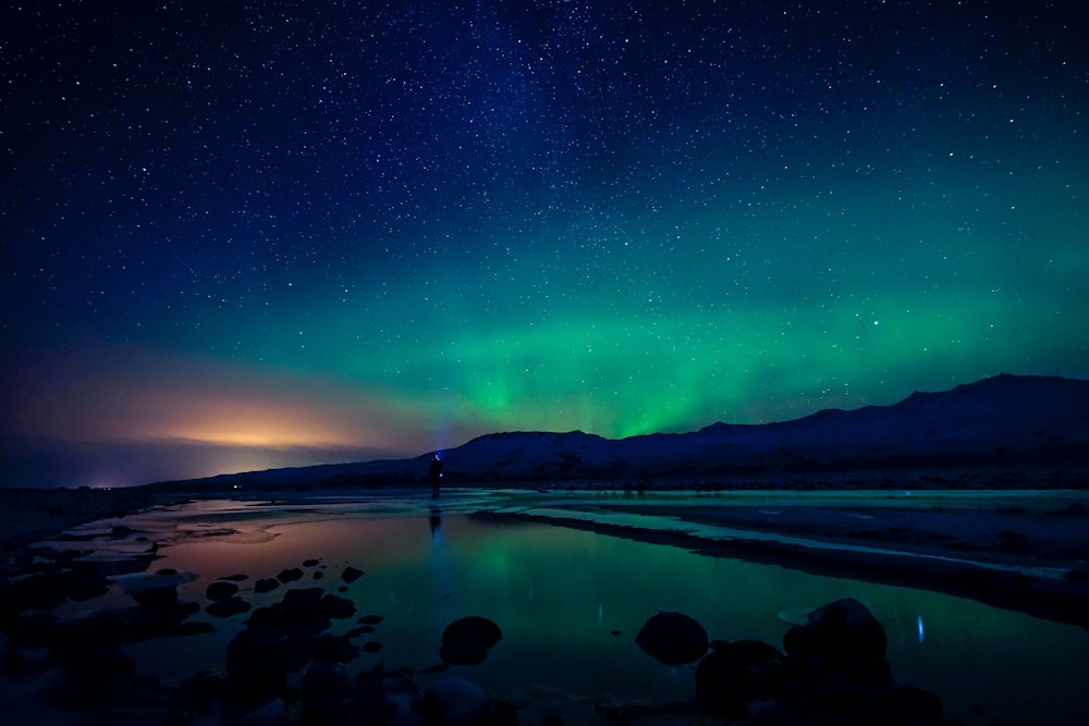 Fotografía de auroras boreales de cuerpo de agua y montaña