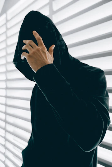 A person in a black hoodie with a hand covering their face