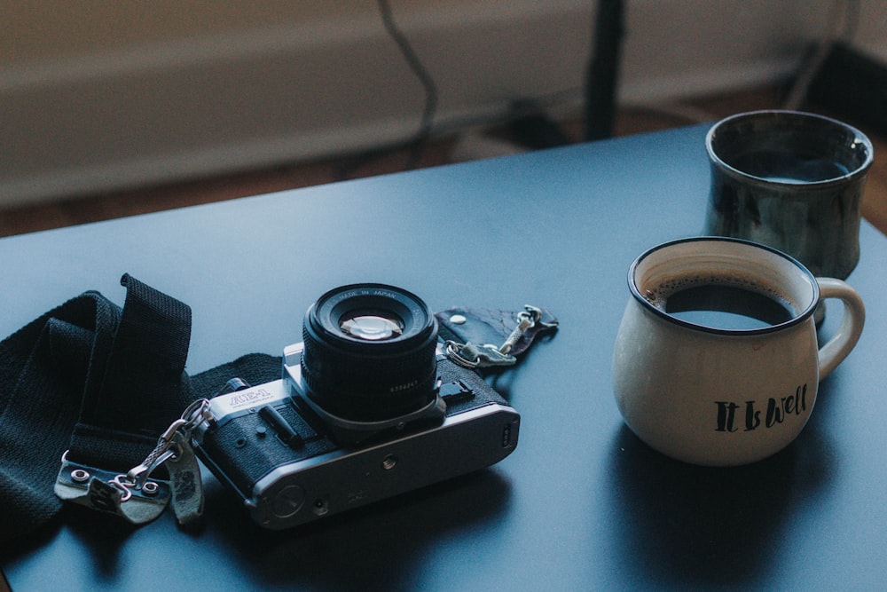 black DSLR camera beside ceramic cup filled with coffee
