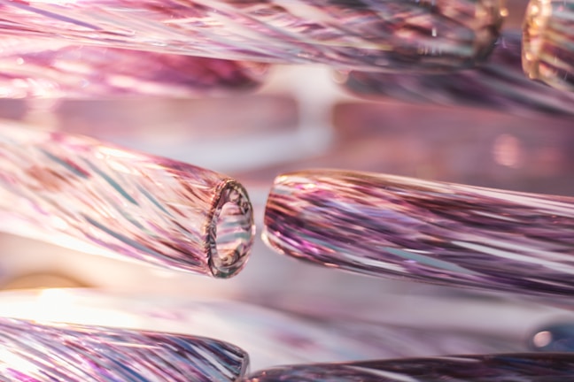 Close-up view of intricately detailed glass rods featuring a swirling pattern with a glossy finish. The rods exhibit a blend of colors that merge together to create an iridescent effect, emphasizing the delicate craftsmanship.