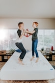 boy and girl jumping on white bed mattress inside room