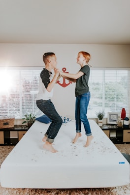 boy and girl jumping on white bed mattress inside room