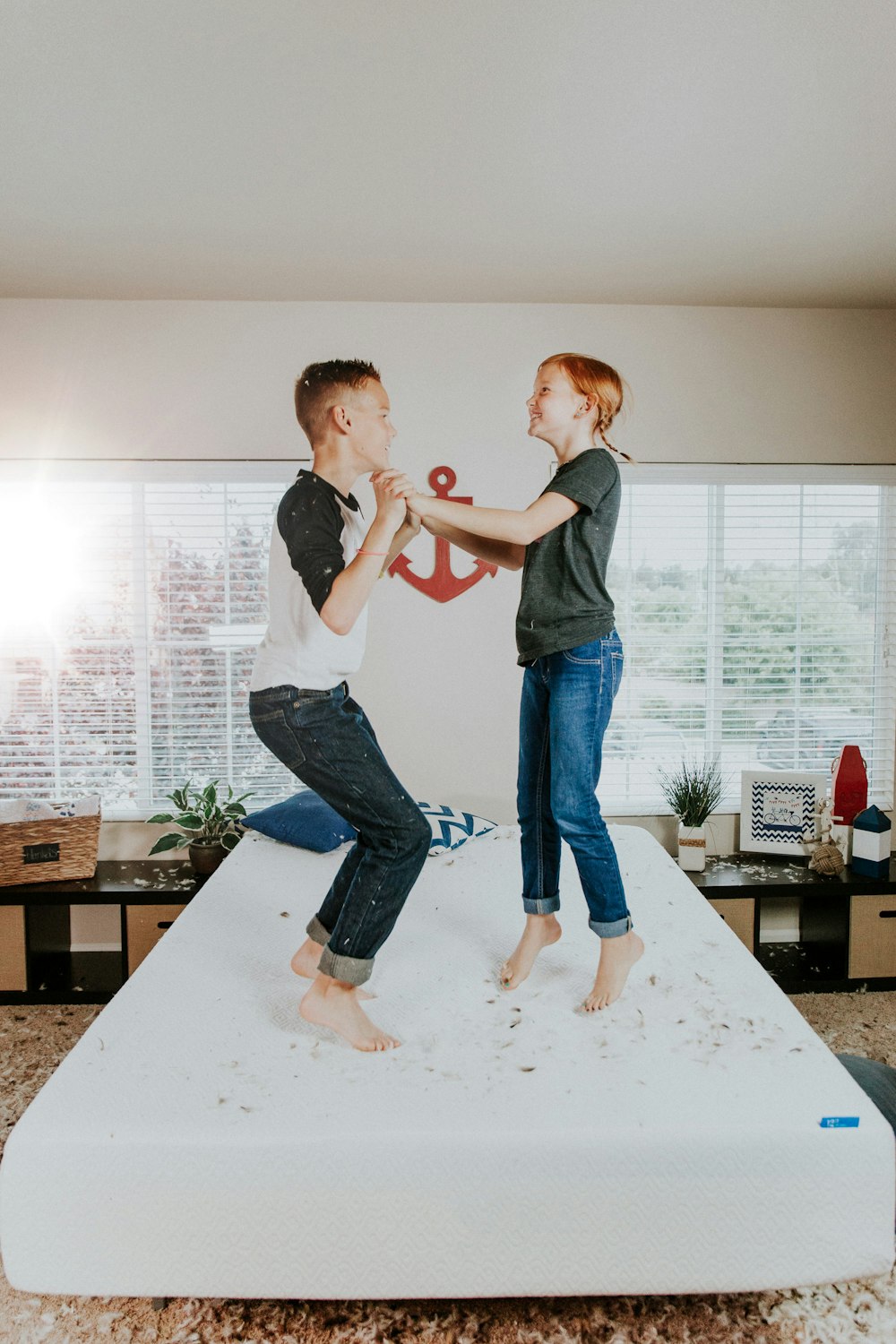 boy and girl jumping on white bed mattress inside room
