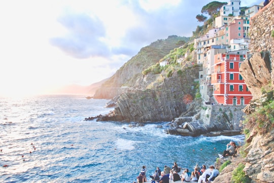 group of people on rock hill near body of water with concrete buildings nearby at daytime in Parco Nazionale delle Cinque Terre Italy