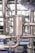 A close-up view of industrial stainless steel piping with clamps and connectors. The machinery appears to be part of a larger industrial system, possibly involving liquid or gas transport. The metal surface has a metallic sheen, and there are several interlocking pipe sections.