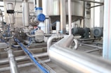 A complex network of industrial equipment featuring shiny metal pipes and machinery, including motors and valves. The setup appears to be part of a processing or manufacturing plant, highlighting various components and instrumentation involved in industrial operations.