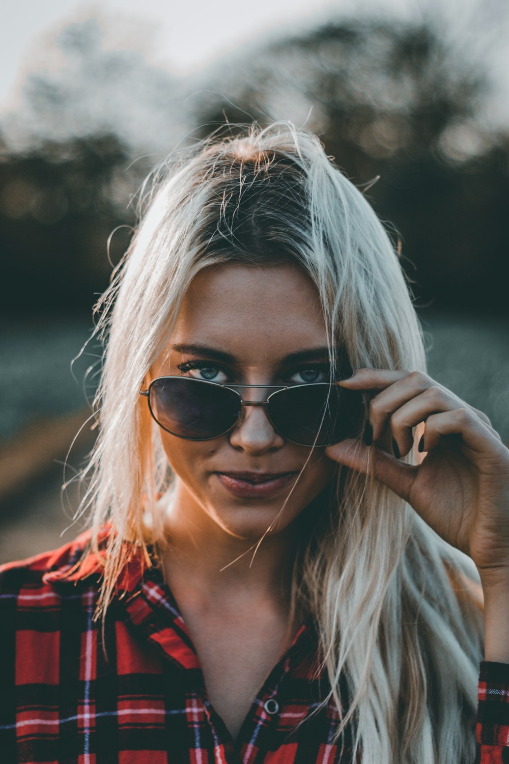 woman wearing red and black plaid top holding sunglasses