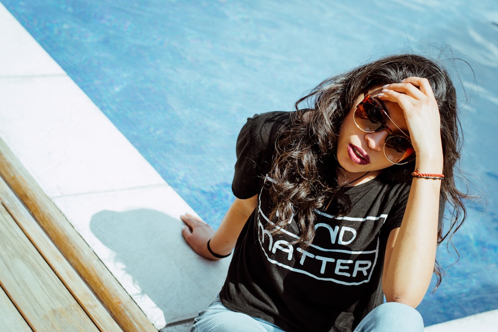 Frau im schwarzen T-Shirt sitzt in der Nähe des Swimmingpools