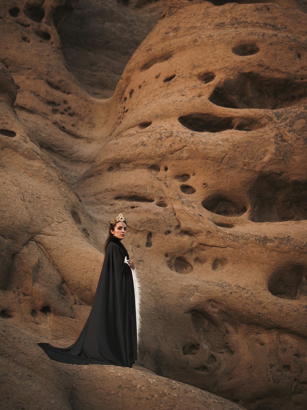 茶色の山の上に立つ黒いマントの女性
