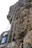 A tall metal ladder is anchored to a rocky cliff, extending vertically from the ground to the top of the rock face. There are some signs attached to the ladder, displaying text in a foreign language. The rocky cliff is rugged and textured, appearing both steep and imposing.