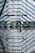 A modern airport terminal featuring large glass walls and strong geometric patterns from the sunlight filtering through. Escalators and information signs are visible, with a lone figure interacting with a digital kiosk. The reflective floor creates an illusion of symmetry and depth.