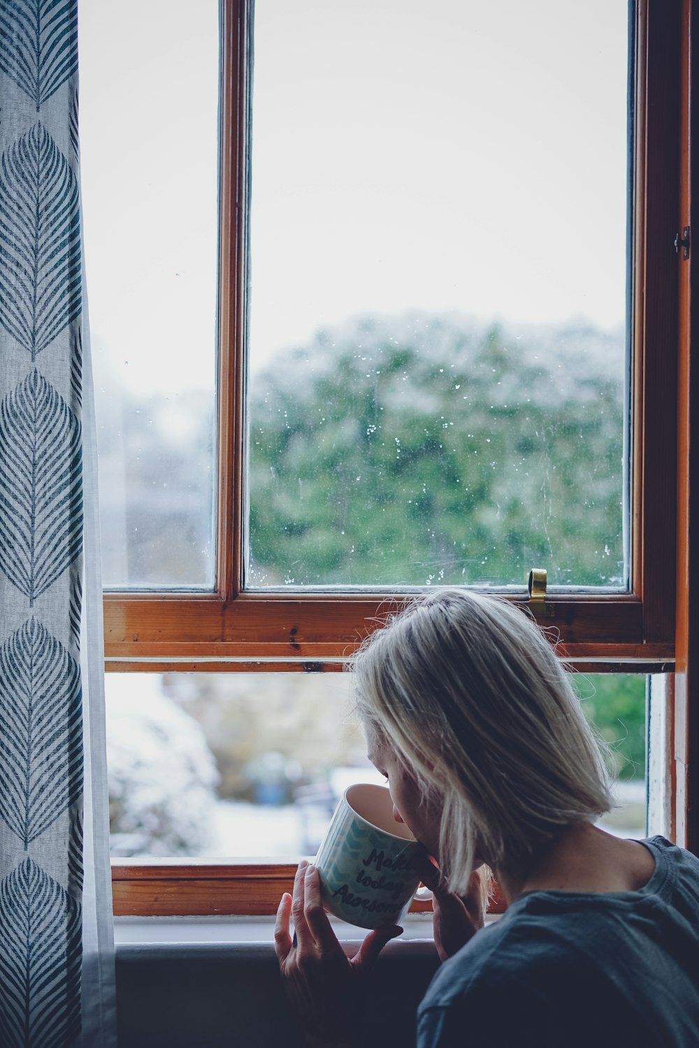 Mujer bebiendo frente a la ventana durante el día