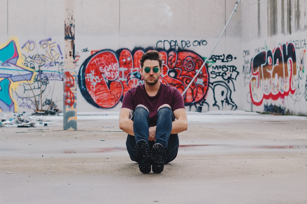 man wearing purple shirt sitting in front of graffiti wall
