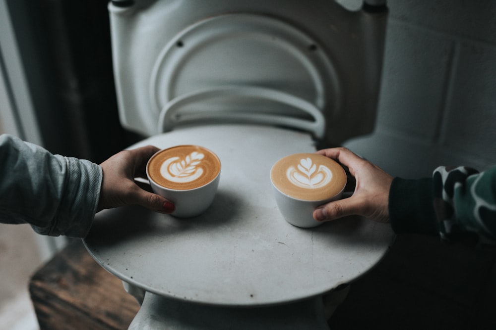 two person holding cappuccino coffee cups