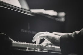 A close-up of a person's hands playing the piano. The image is in black and white, emphasizing the motion and focus on the keys. The piano is a Steinway & Sons model, showing a sense of elegance and quality.