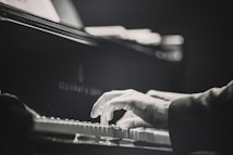 A close-up of a person's hands playing the piano. The image is in black and white, emphasizing the motion and focus on the keys. The piano is a Steinway & Sons model, showing a sense of elegance and quality.