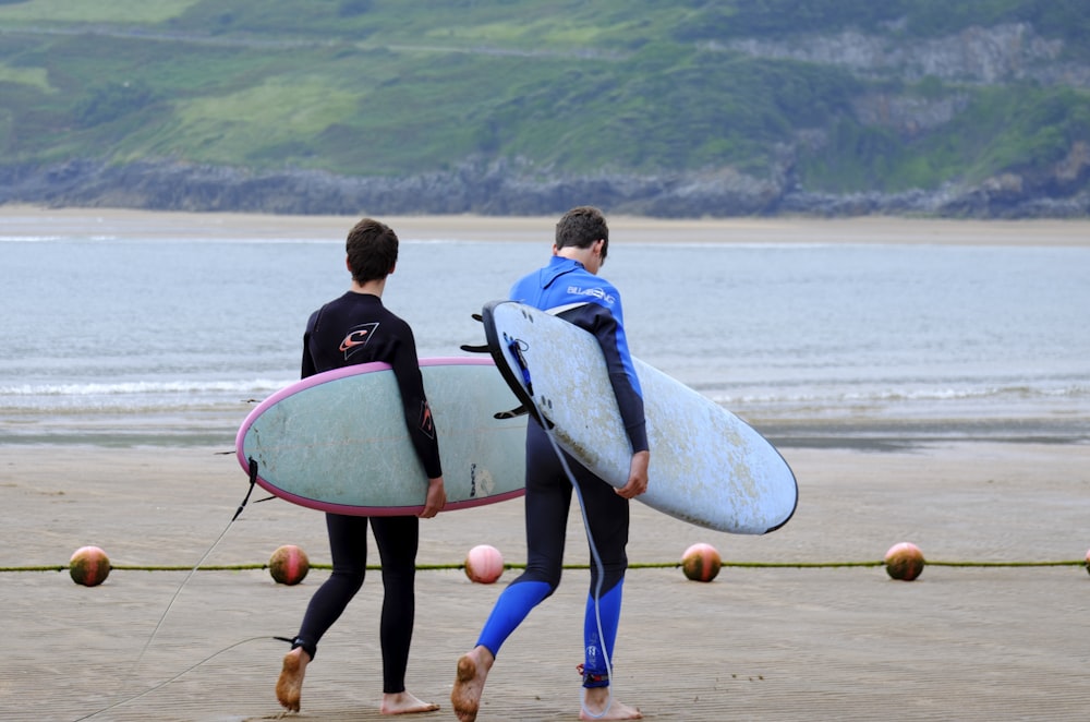 two men walking on the seashore carrying surfboards