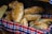 A basket filled with freshly baked loaves of bread. The bread has a golden-brown crust and is arranged on a colorful, checkered cloth.