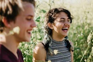 man and woman laughing surrounded with green grass during daytime
