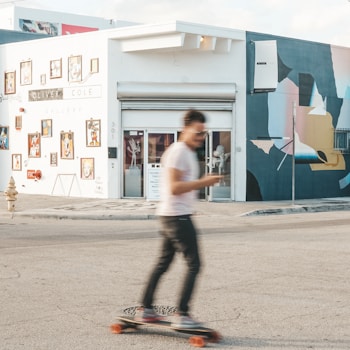 Man riding a longboard past a teal building
