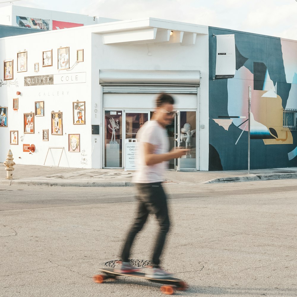 man using longboard near white and teal structure during daytime