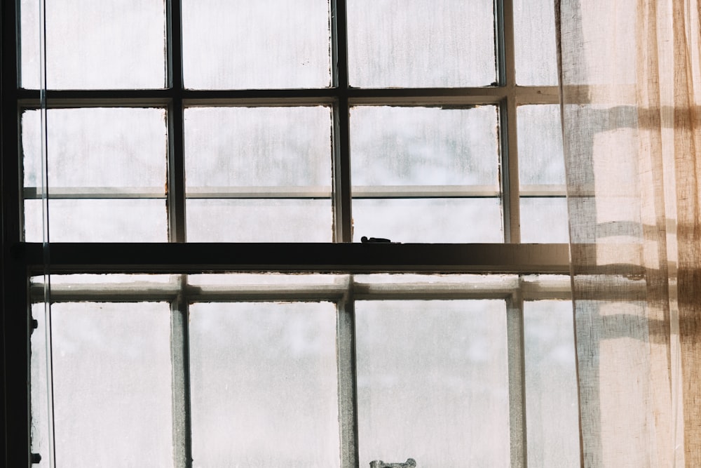 um gato sentado no parapeito de uma janela em frente a uma cortina